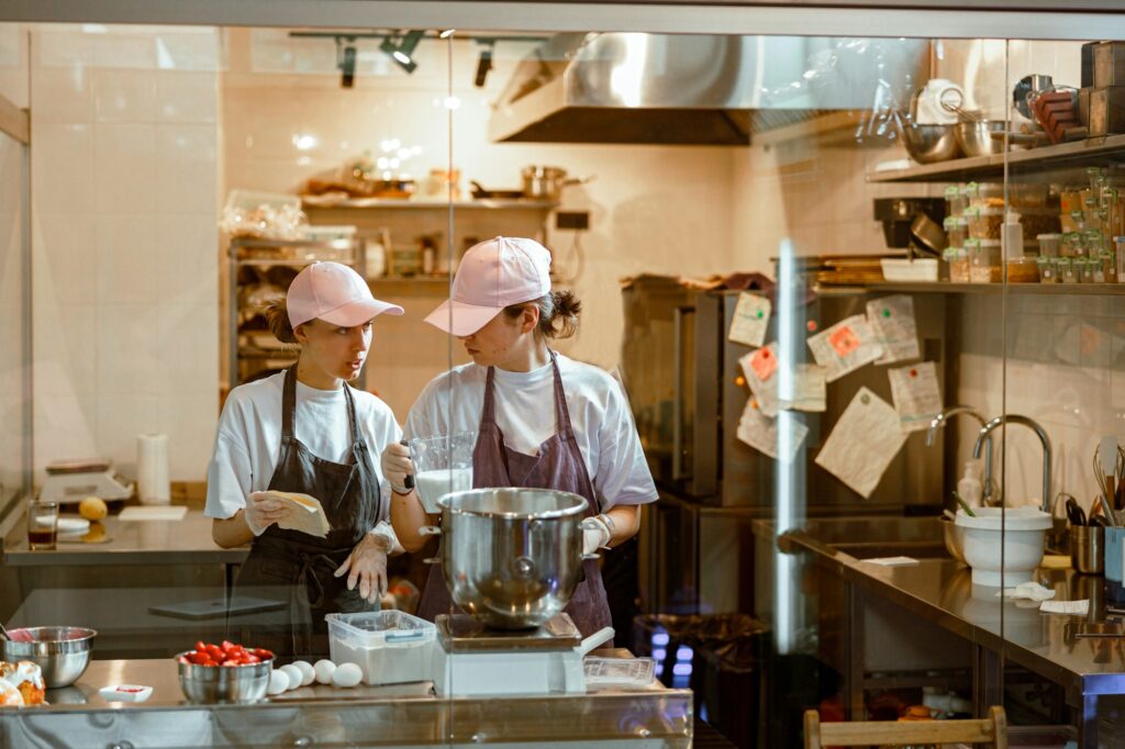 Woman shows recipe to colleague making dough at table in bakery